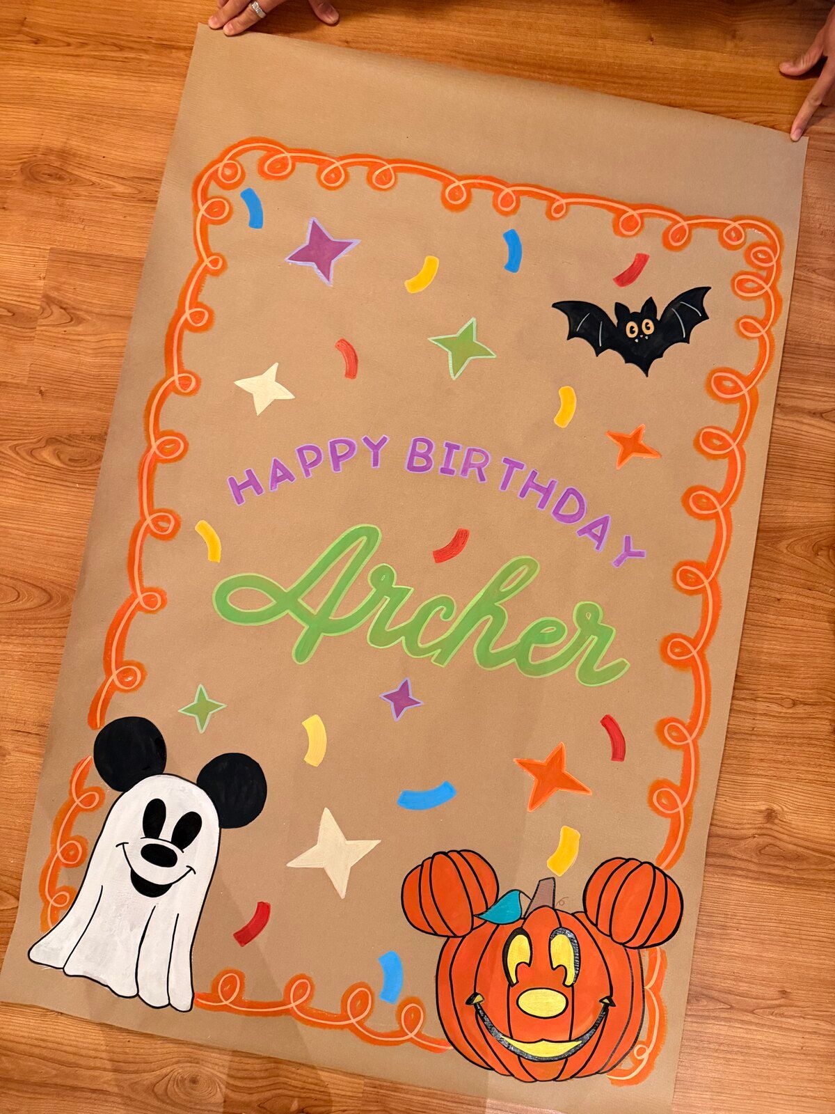 The “Happy Birthday Archer” Halloween banner on a wooden floor, held flat at its top corners.