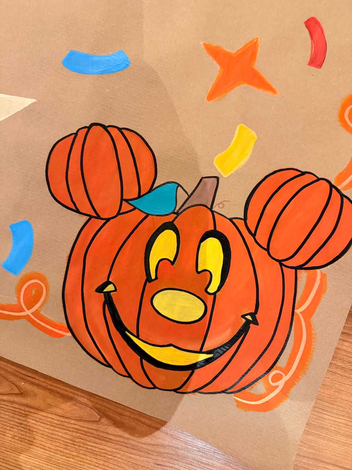 Close-up of the Halloween banner’s jack-o’-lantern: an orange pumpkin with mouse ears and a smiling yellow face, surrounded by confetti.
