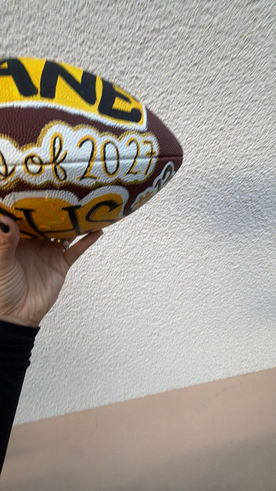 The painted football tilted up and partly out of frame, showing the gold name panel and “of 2027” in script.